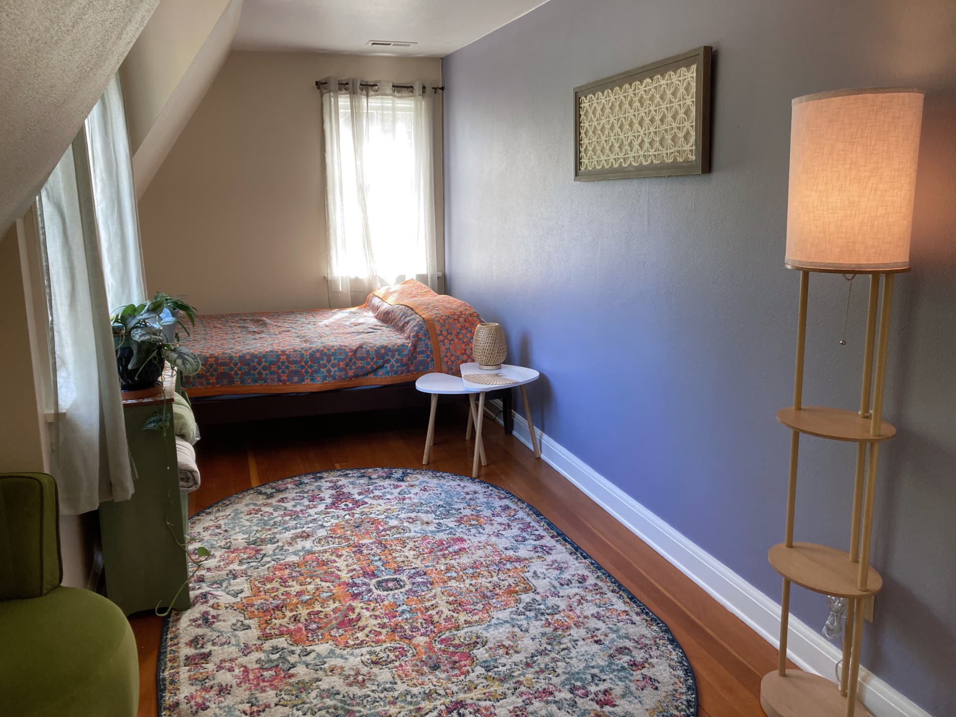 cozy private room containing a bed with orange and blue patterned bedding and a bookshelf with potted plants