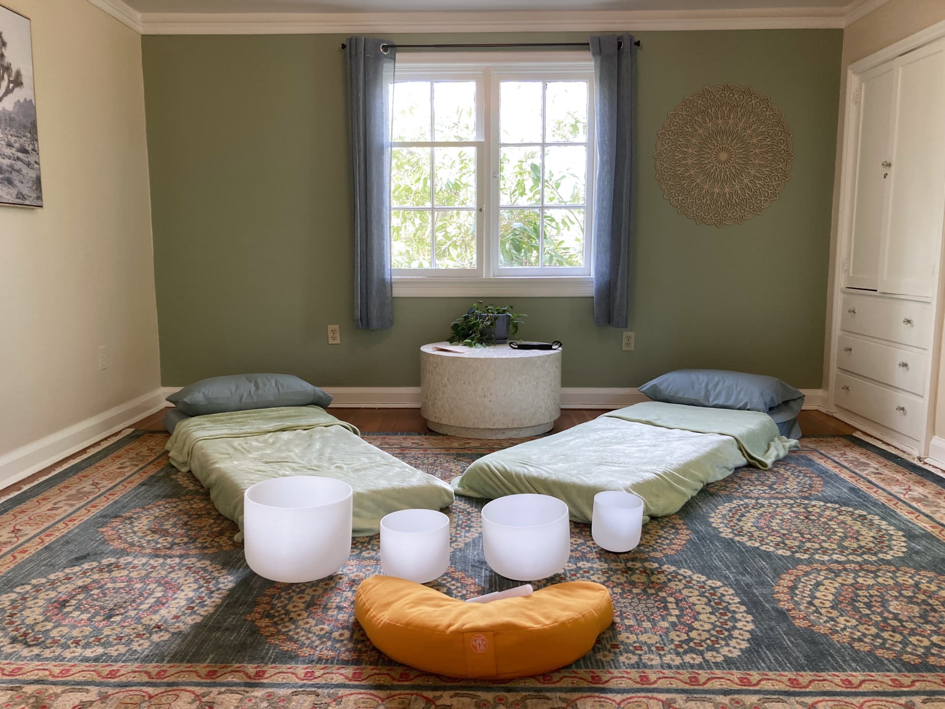 large group room with floor pads and a meditation cushion next to four white glass singing bowls